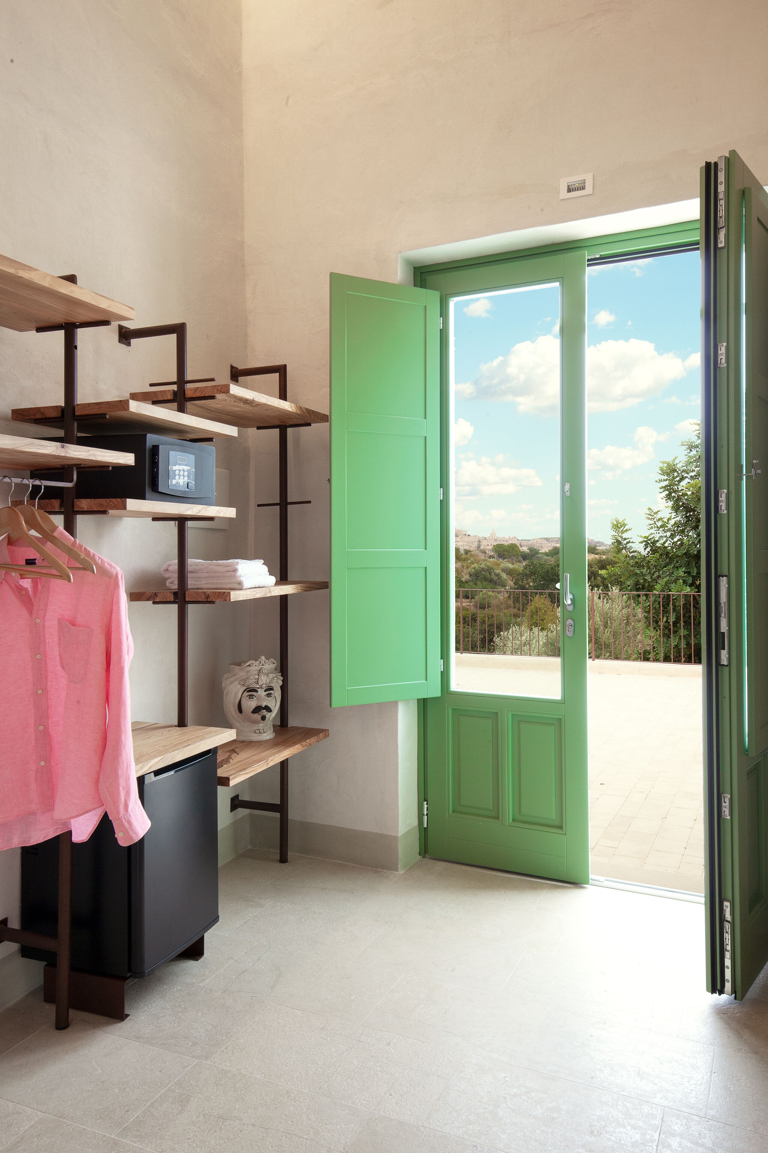 A room with a green door, a black cabinet, and wooden shelves with various items.