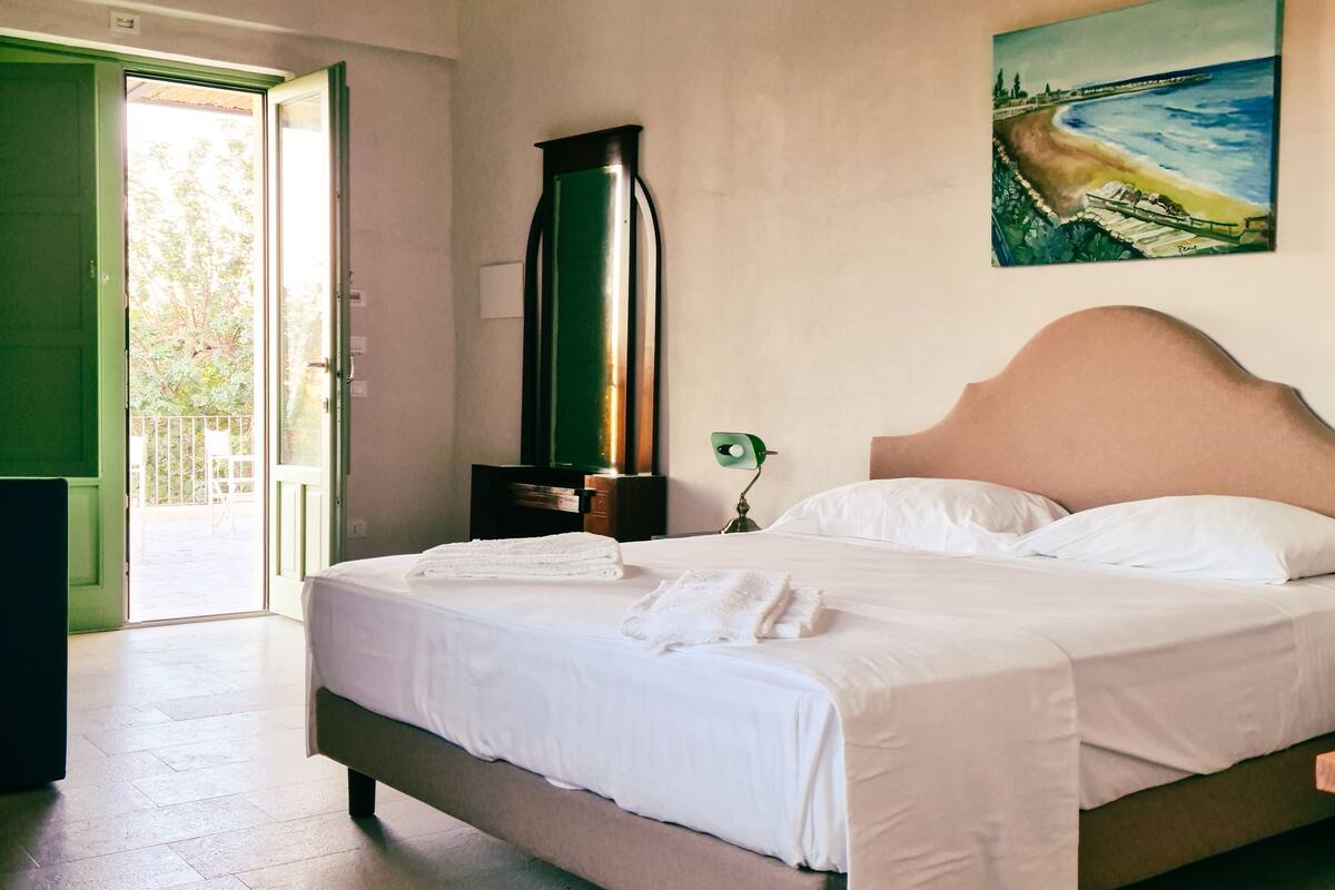 Un dormitorio con una cama, una silla verde, un cuadro y un radiador.