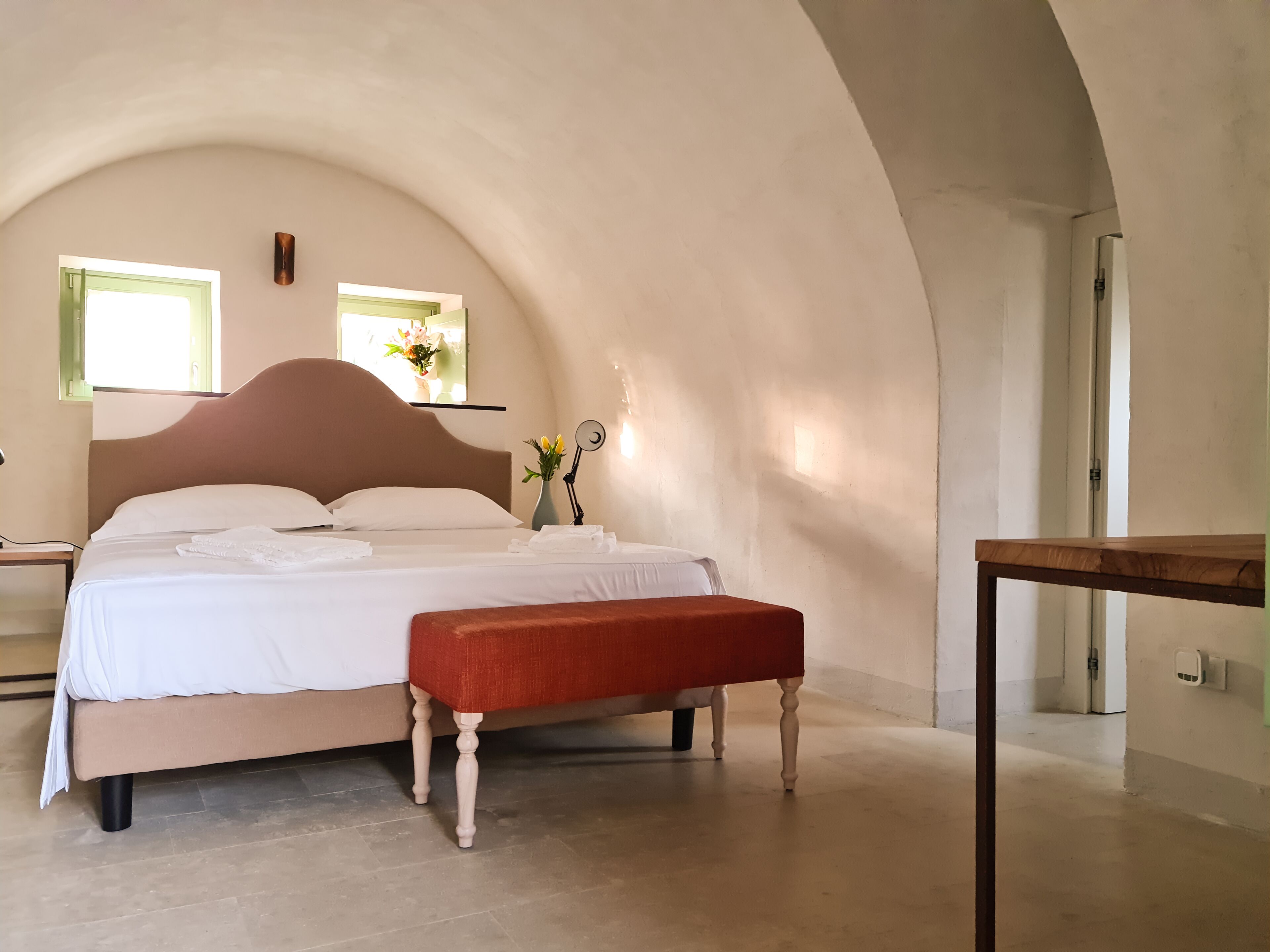 A bedroom with a large bed, a bedside table, a small table, and a bench.