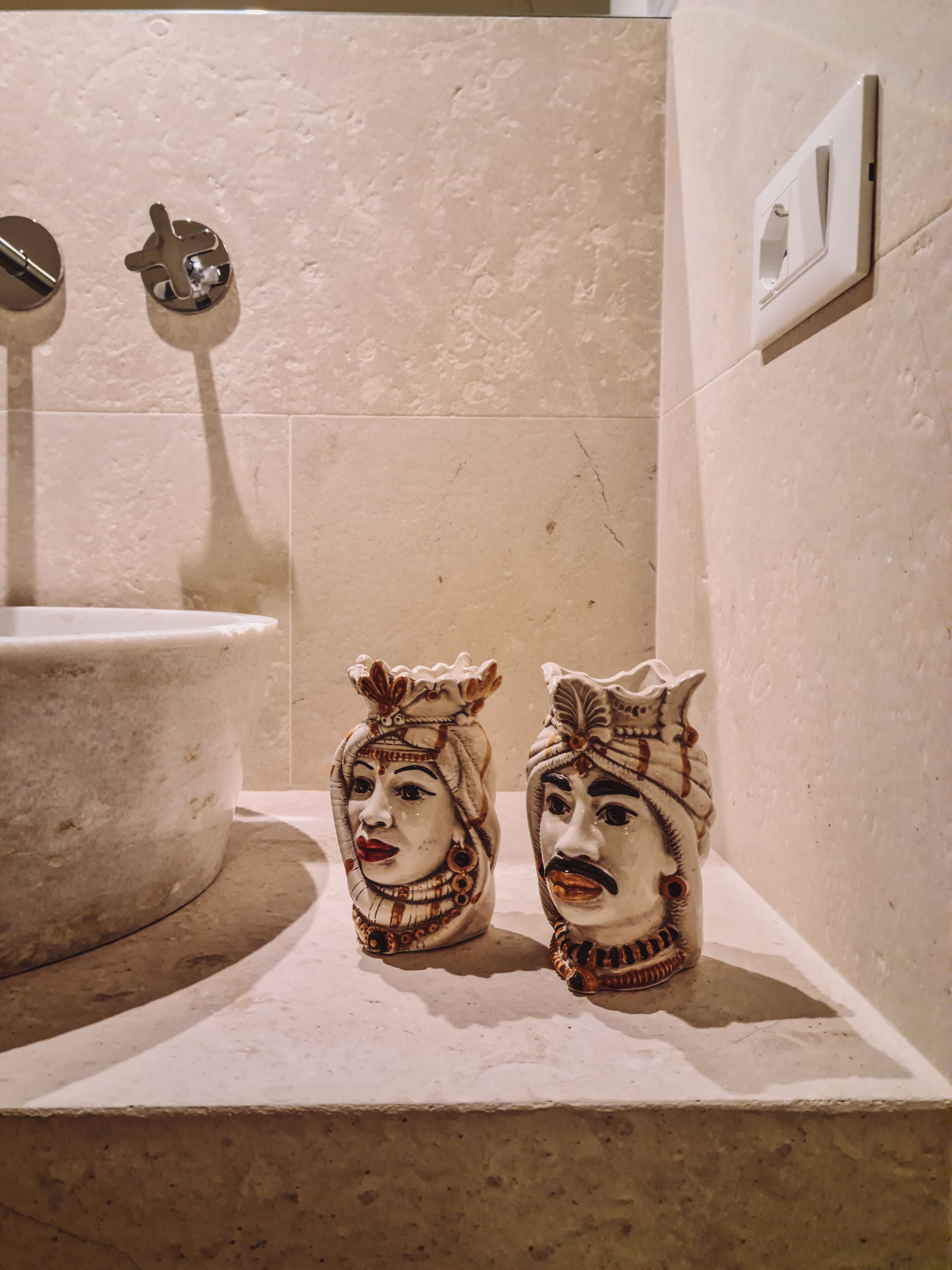 Ein Badezimmer mit Waschbecken, einem Spiegel und zwei dekorativen Masken auf einem Regal.
