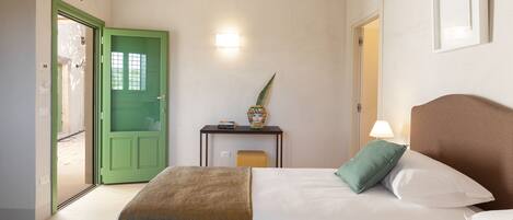 Quarto de hotel com duas camas, uma porta verde, uma mesinha com luminária e uma luz na parede.