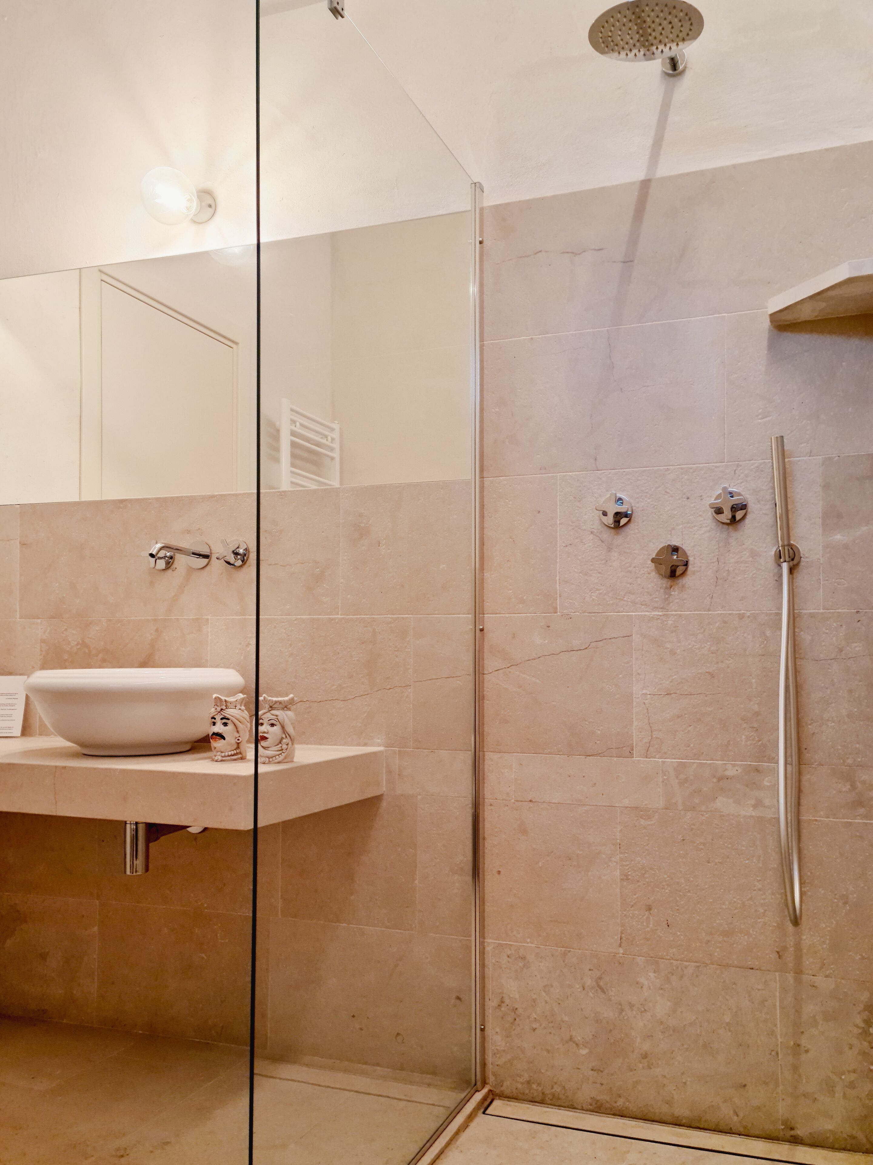Un baño moderno con ducha de vidrio, un lavamanos con posavasos decorativo y un espejo sobre el lavamanos.