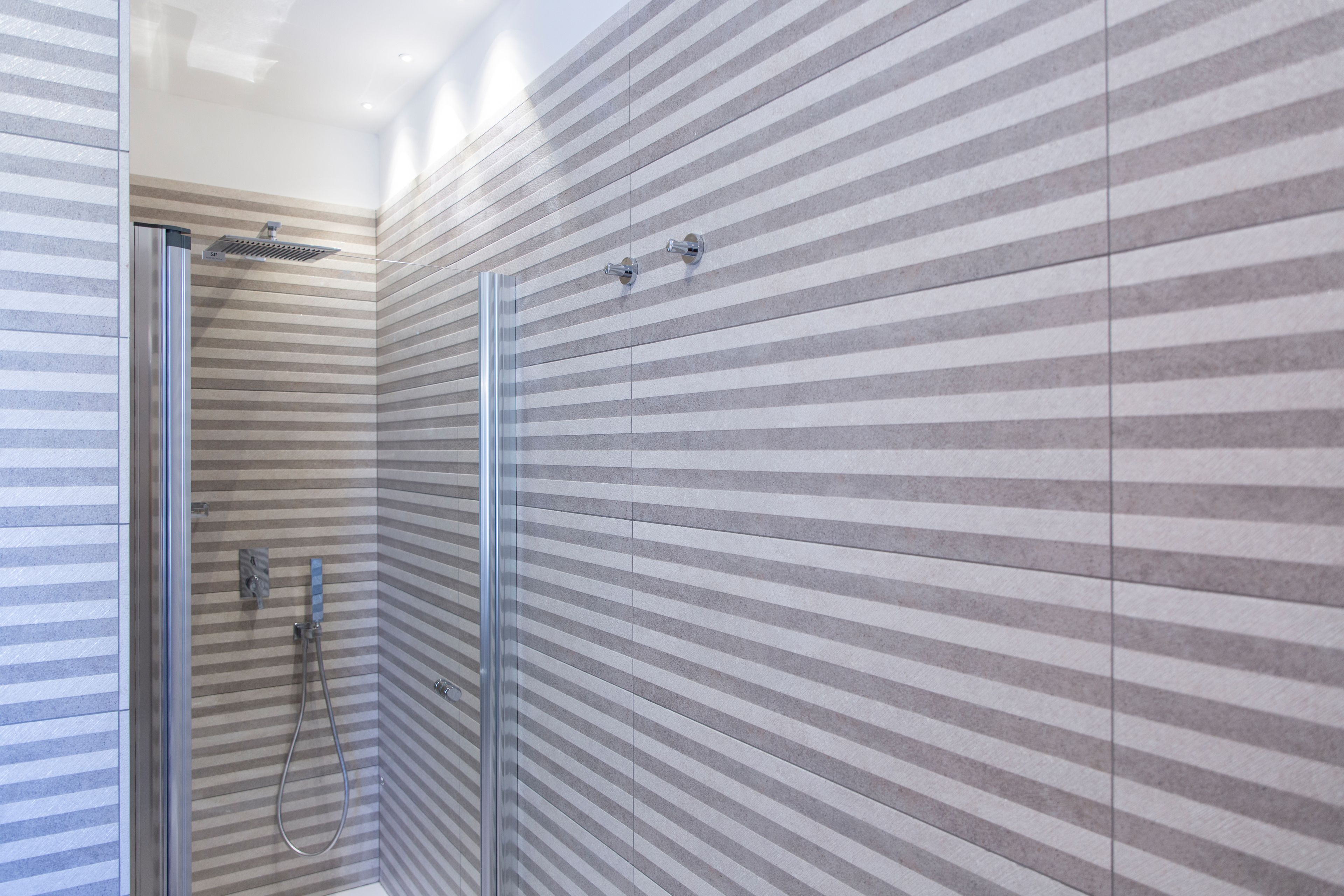 A modern bathroom with striped tile walls, a glass shower enclosure, and a visible showerhead.