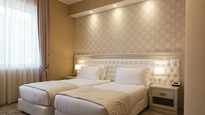 A hotel room with two beds, a headboard with a geometric pattern, bedside lamps, and a nightstand with a drawer. - Aurum Suites (Pescara)