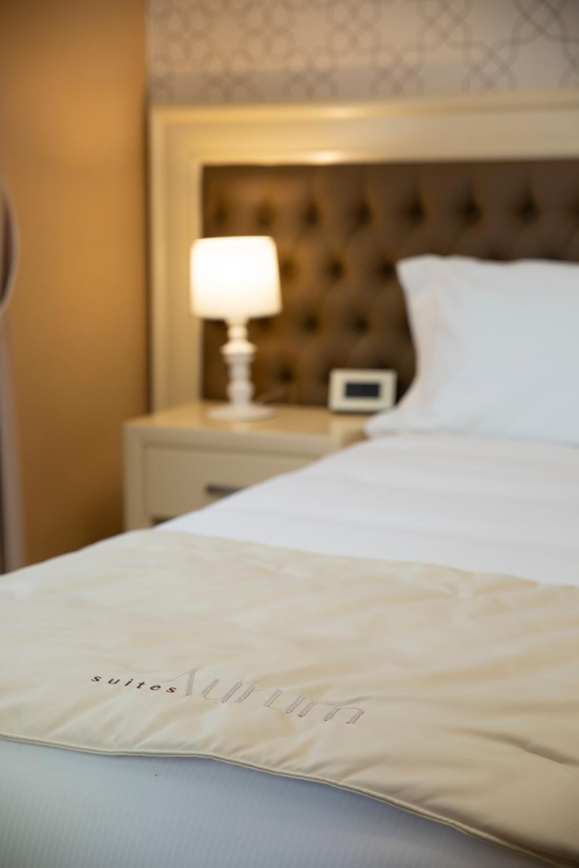 A hotel room with a neatly made bed, a bedside lamp, and a small bedside table with a clock.