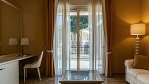 A hotel room with a glass-top table, a sofa, a desk with lamps, and a view of a building through sheer curtains. - Aurum Suites (Pescara)