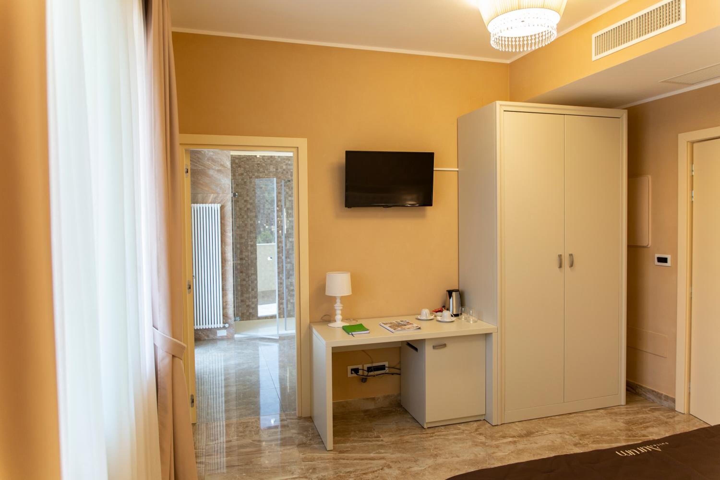 A hotel room with a bed, a desk with a lamp, a television, and a wardrobe.