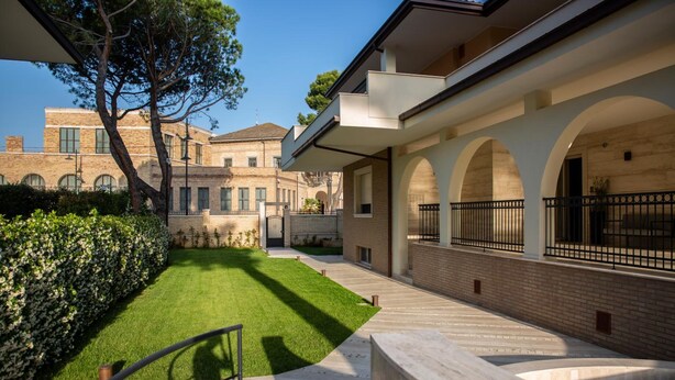 A courtyard with a well-maintained lawn, a stone pathway, and a building with arched windows and a balcony. - Aurum Suites (Pescara)