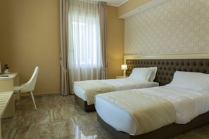 Habitación de hotel con dos camas, un escritorio, una silla y un ventanal con cortinas.