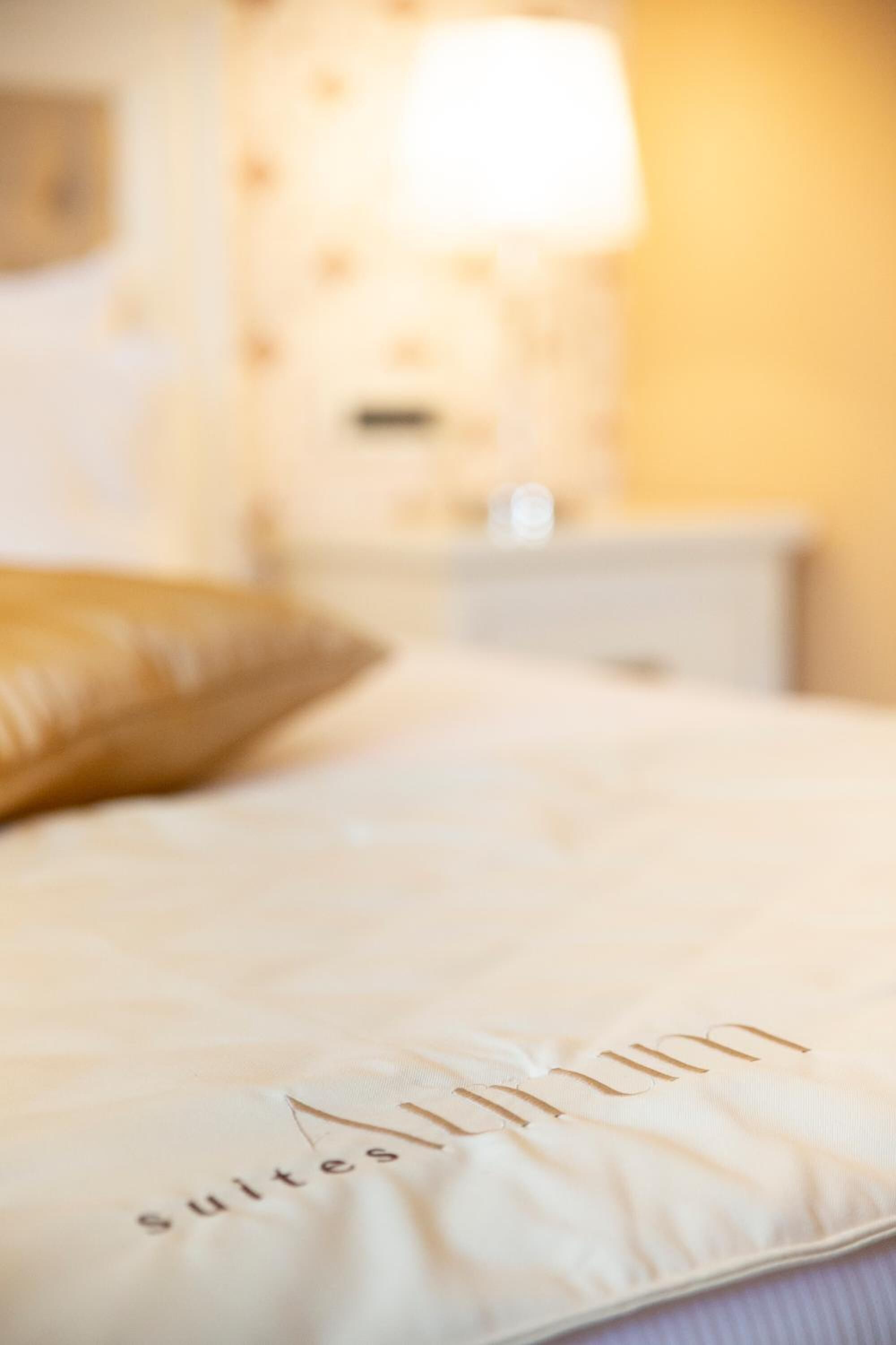 Un lit avec un oreiller portant l’inscription « Suites » et une table de chevet avec une lampe.