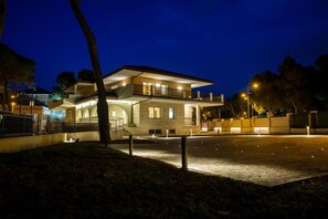 Una casa moderna de dos pisos con balcón, entrada para vehículos e iluminación exterior brillante en la noche.