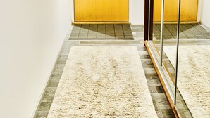 Un pasillo con dos puertas de madera, una alfombra blanca y un espejo que refleja las puertas.