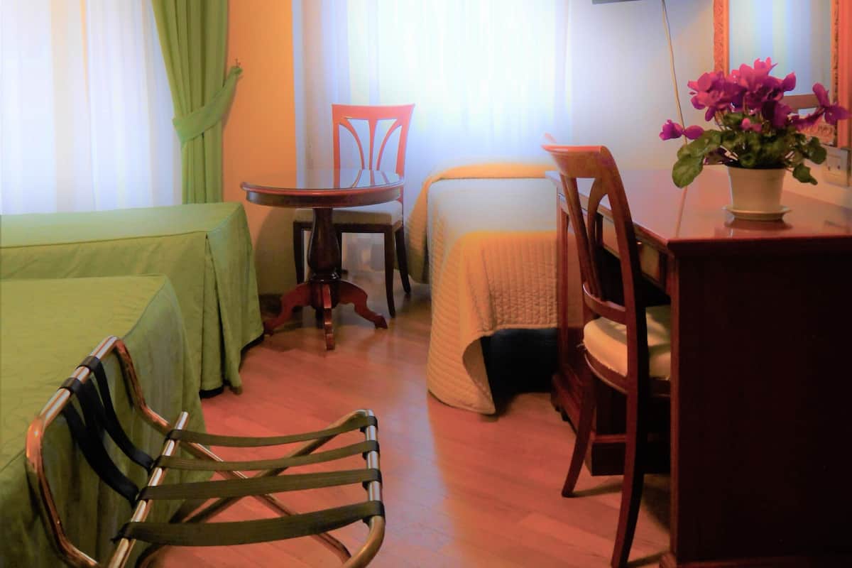 A hotel room with a bed, a desk with a chair, a television, and a window with curtains.