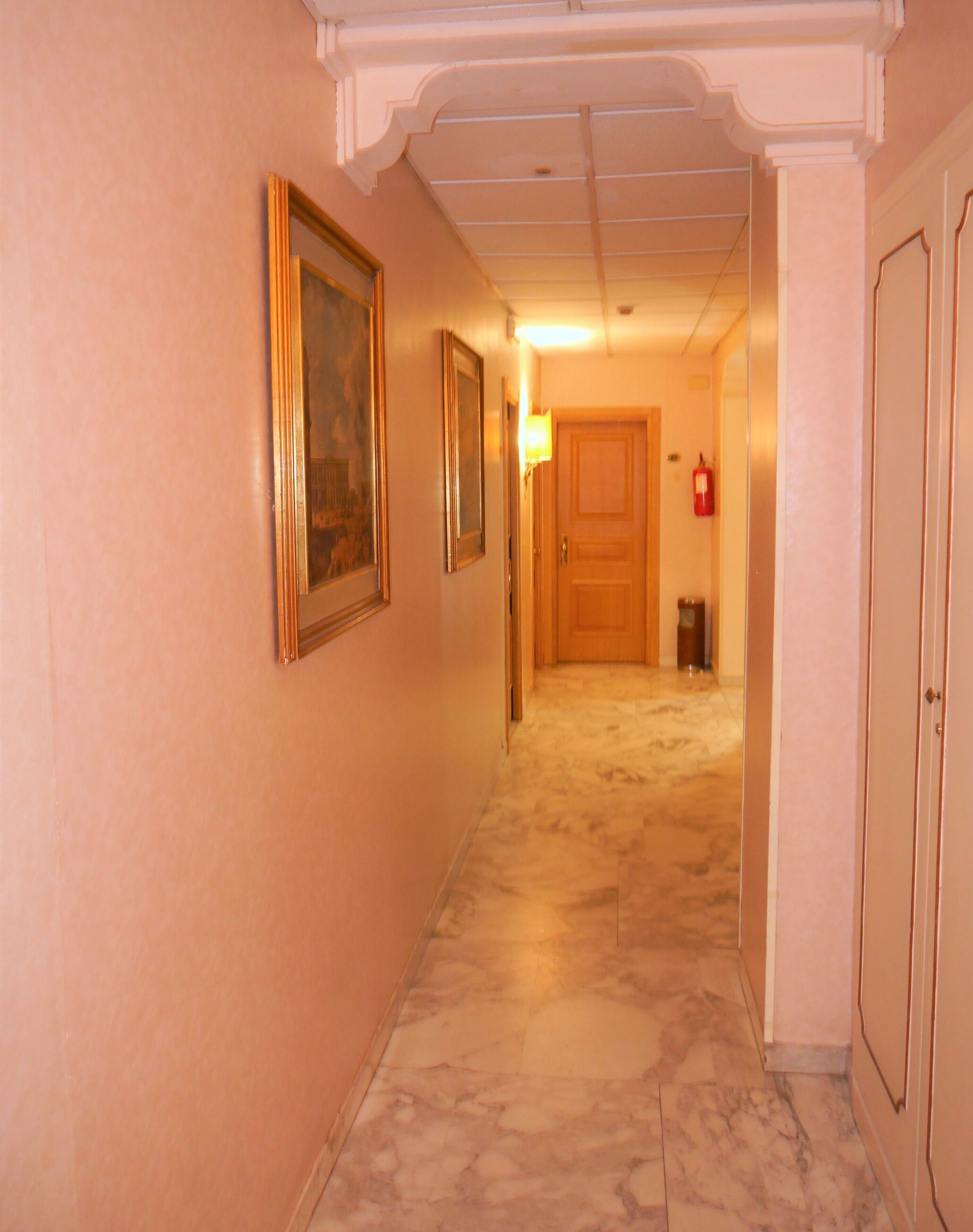 A hallway with marble flooring, framed artwork on the walls, and a door at the end.