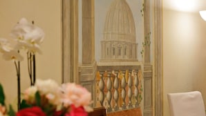 A dining table with a dessert display, a vase of flowers, and a mural of a building. - Hotel San Pietro (Rome)