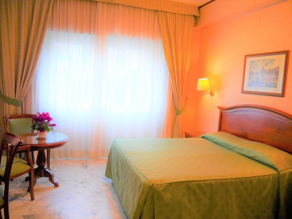 A hotel room with a bed, a chair, a small table with a vase of flowers, a lamp, and a painting on the wall. - Hotel San Pietro (Rome)