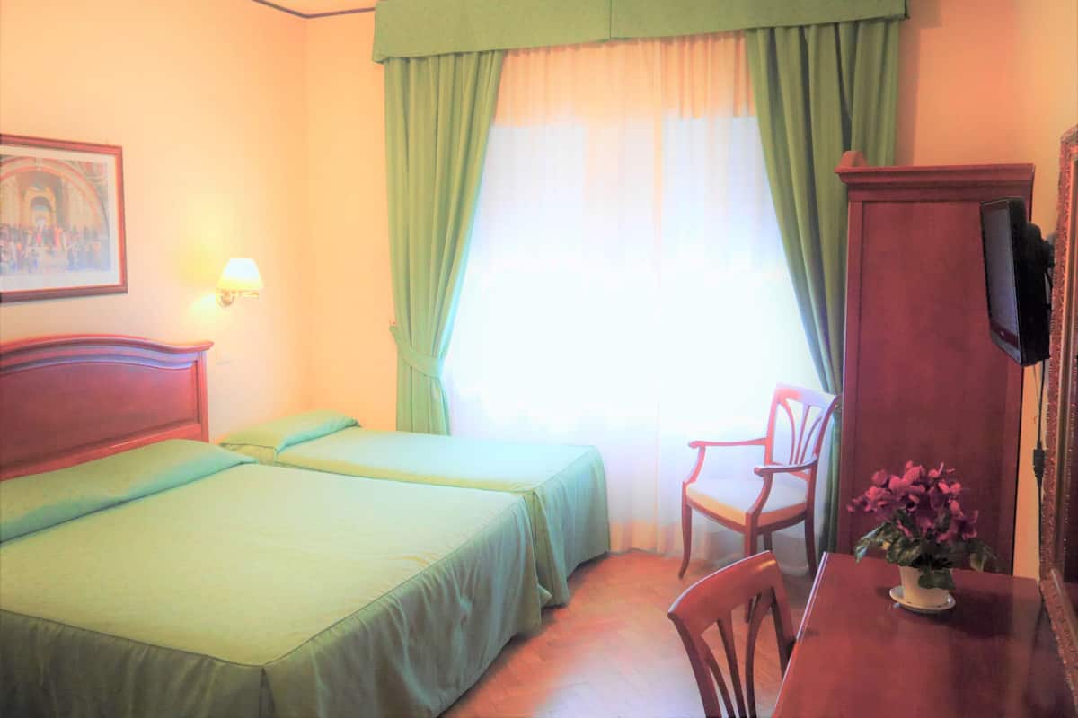 A hotel room with two beds, a desk with a chair, a television, and a painting on the wall.