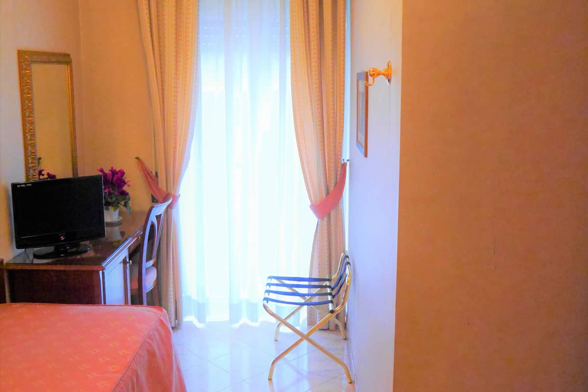 A hotel room with a bed, a desk with a computer, a chair, and a window with curtains.