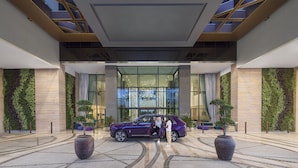 Une entrée moderne, avec une voiture de luxe violette garée devant, de grands pots de plantes et une façade en verre.