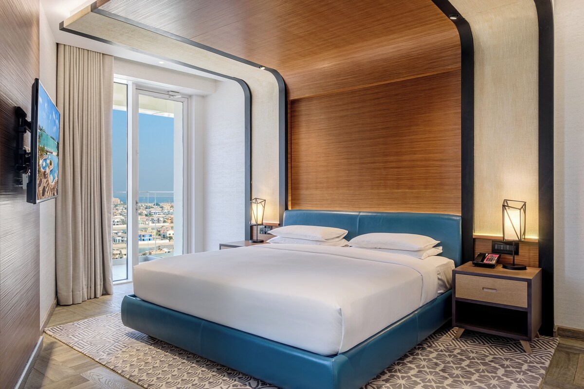 A modern hotel room with a large bed, a city view, and a wooden ceiling.
