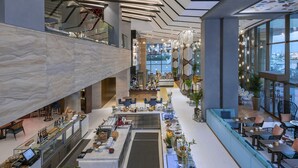 Un hall d’hôtel moderne avec un comptoir d’accueil en marbre, des espaces de détente et une vue sur la ville.