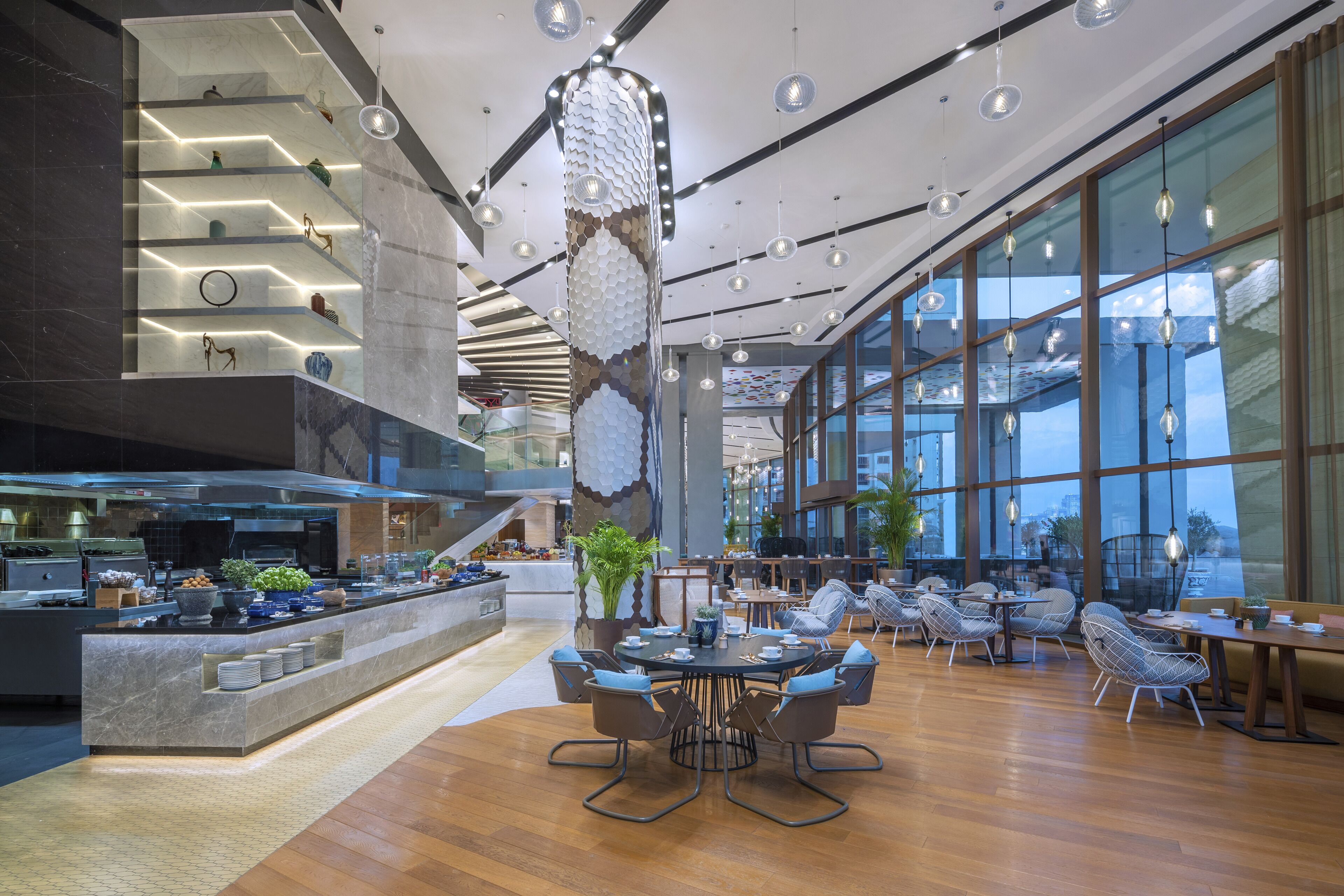 Un moderno vestíbulo de hotel con un comedor central, una cocina y grandes ventanales con vistas.