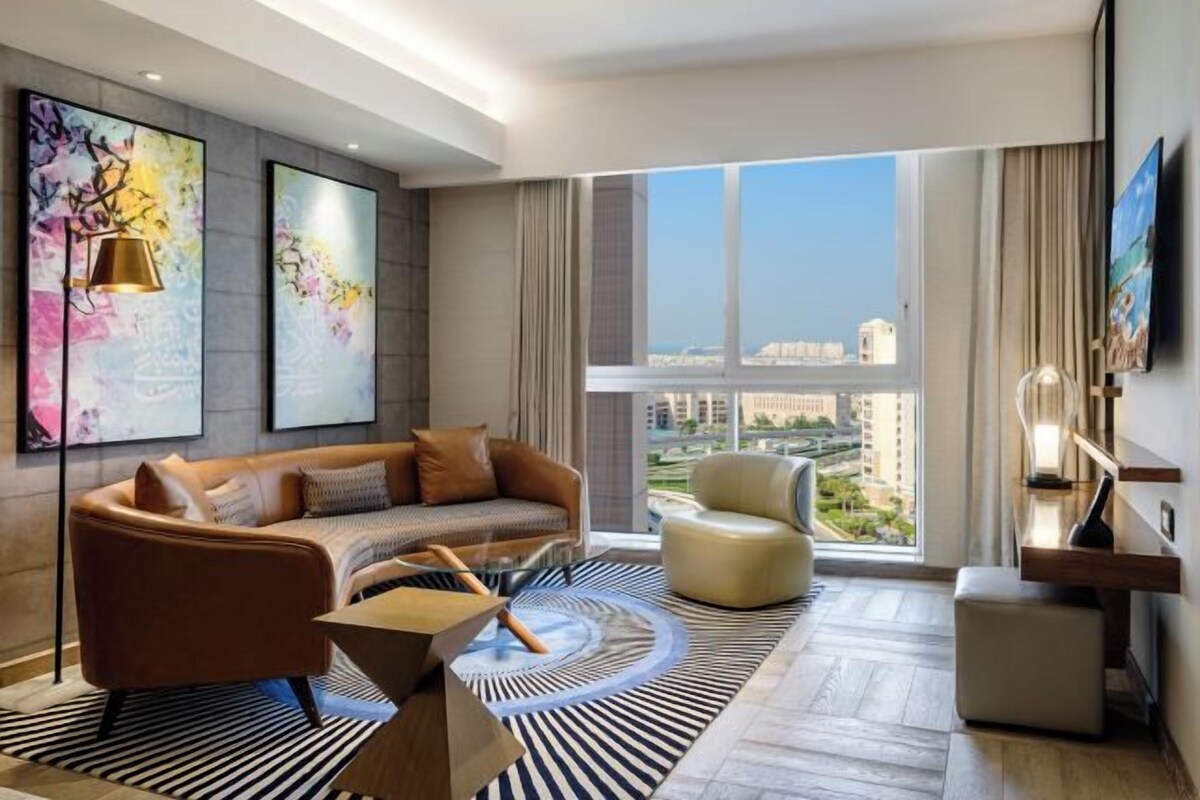Una sala de estar moderna con un sofá, un sillón y una mesa de centro. Amplias ventanas con vistas a la ciudad.