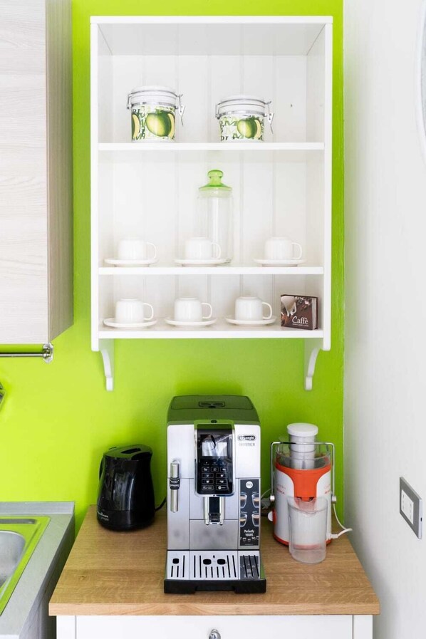 A kitchenette with a coffee machine, a water dispenser, and a cabinet with jars and cups.