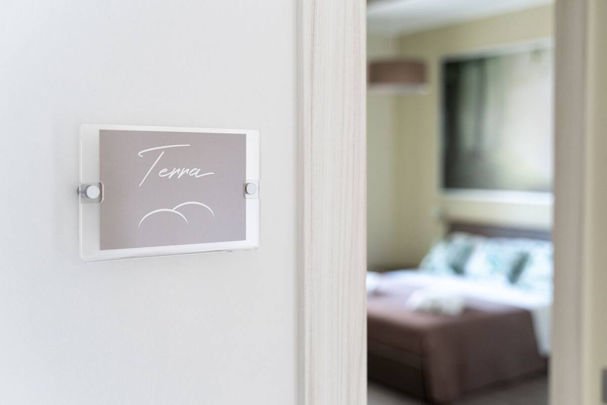 A framed sign with the name "Terra" on a white wall, leading to a bedroom with a bed and pillows.