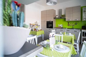 A modern kitchen with light wood cabinets, a green wall, and a dining area with white chairs and green tablecloths. - Baldacci Bed & Breakfast (Pescara)