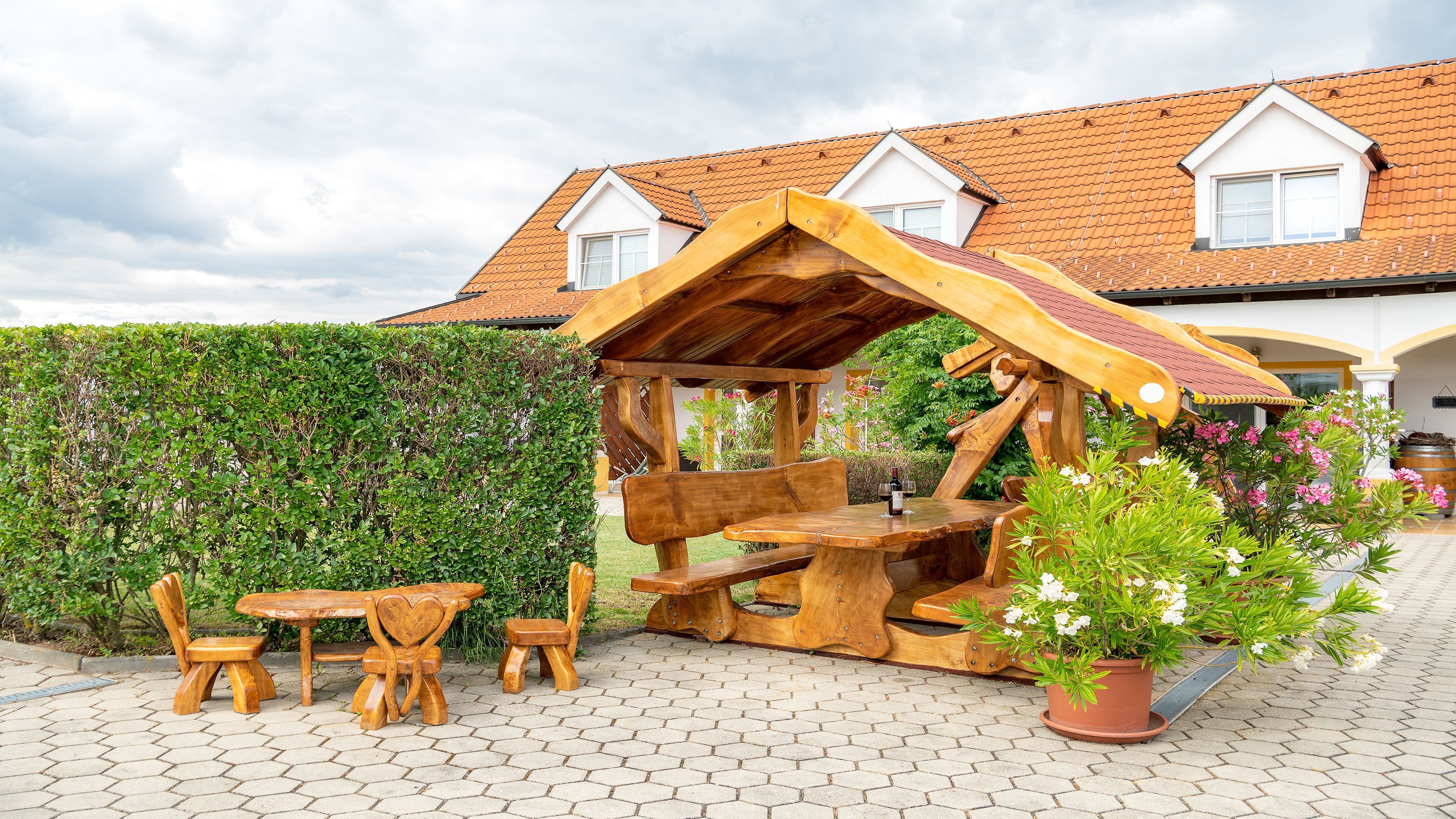 Un área de estar al aire libre con madera, una mesa, sillas, una estructura de madera con techo inclinado y una planta en maceta.