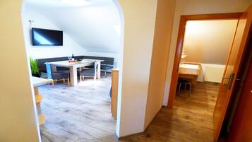Ein schmaler Flur führt zu einem Essbereich mit Tisch und Stühlen, einem an der Wand befestigten Fernseher und einem Holzboden.