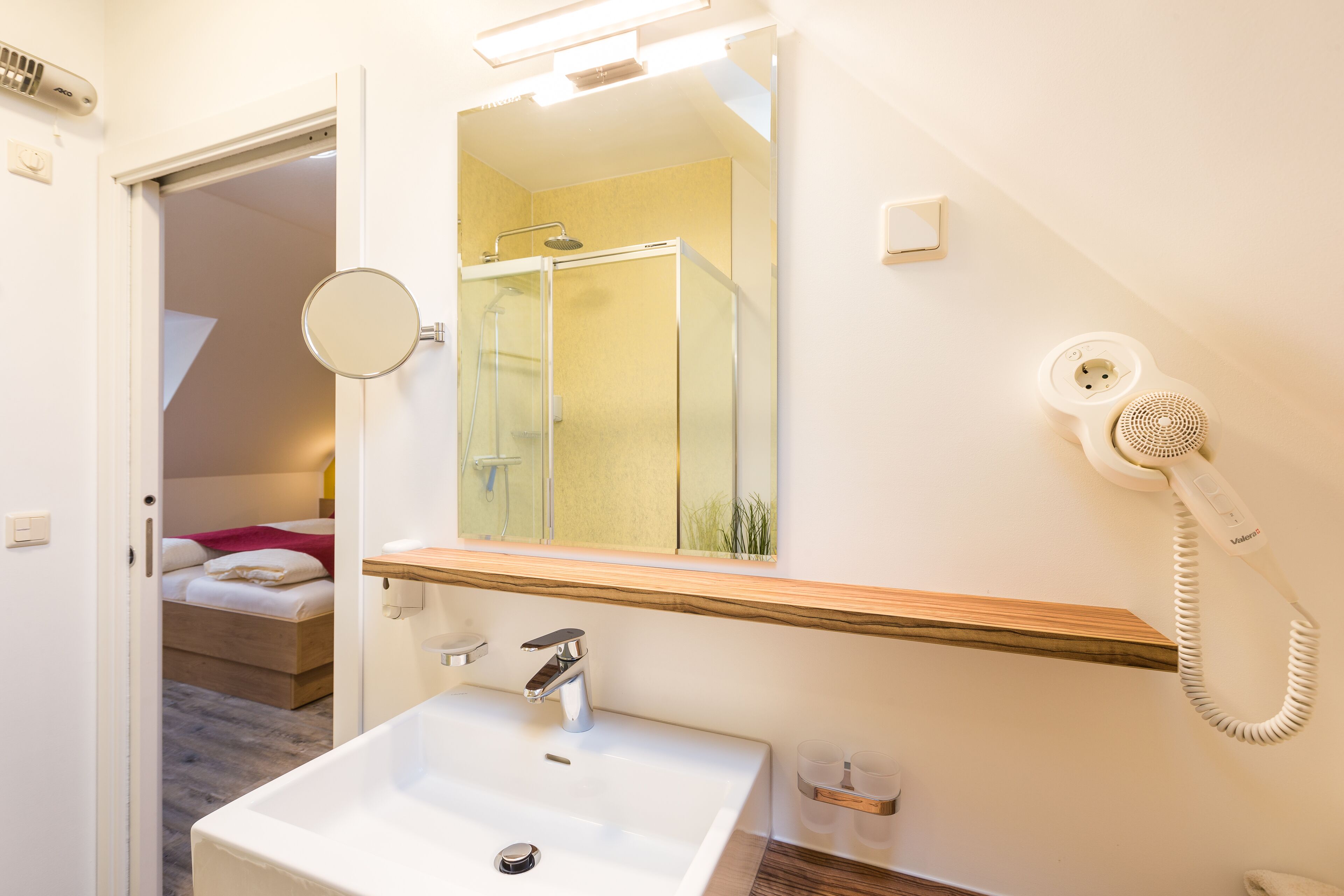 Een badkamer met een wastafel, spiegel en een haardroger aan de muur.