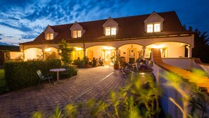 A large house with multiple windows, a covered patio, and a well-lit entrance. - Appartementhaus Martina (Morbisch am See)