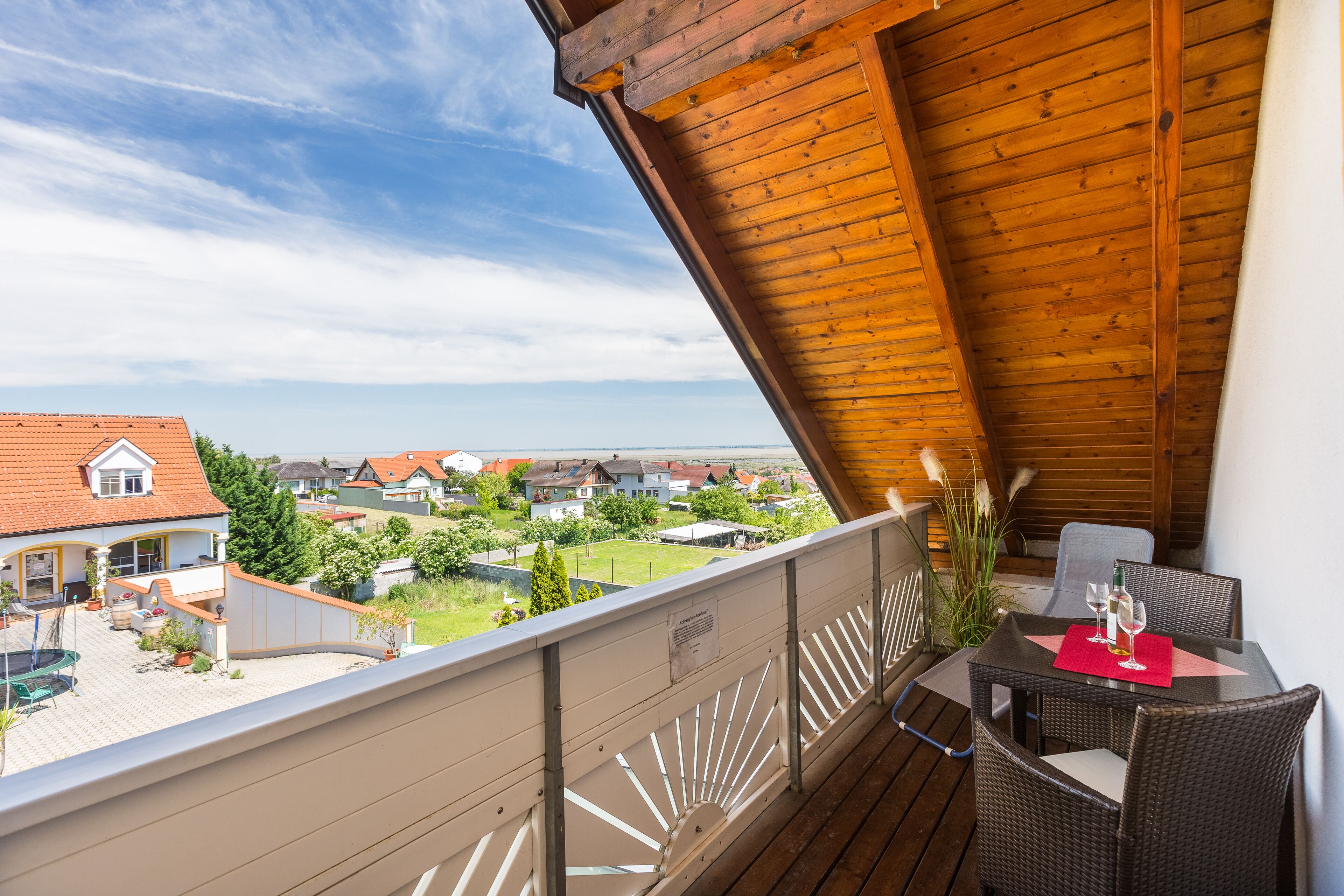 Ein Balkon mit Holzboden, Korbmöbeln und einem Tisch, gedeckt mit Weingläsern und einer Flasche.