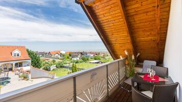 Ein Balkon mit Holzboden, Korbmöbeln und einem Tisch, gedeckt mit Weingläsern und einer Flasche.