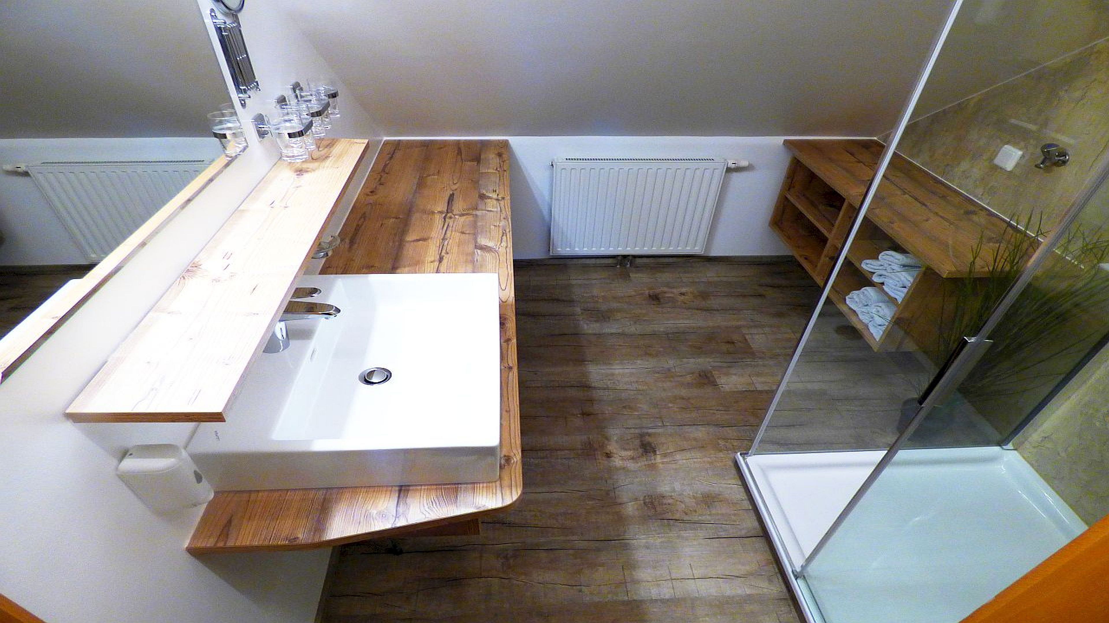 A bathroom with a wooden vanity, a white sink, and a glass shower enclosure.