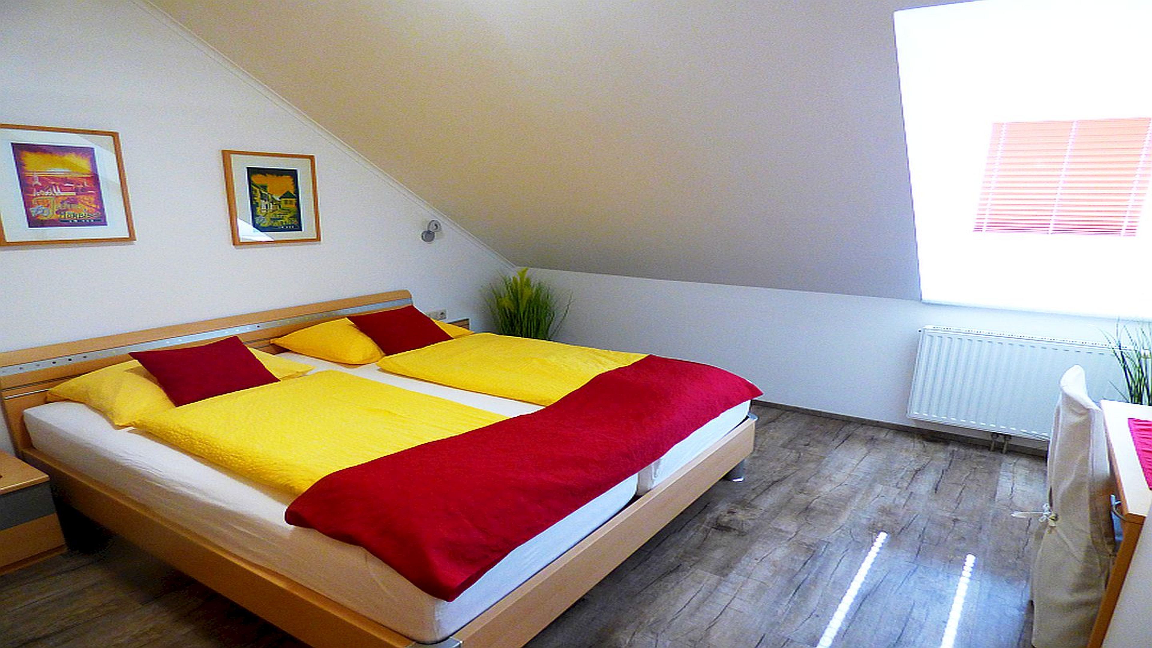 Un dormitorio con cama, dos almohadas, una mesita de noche, un radiador y una ventana con persianas.