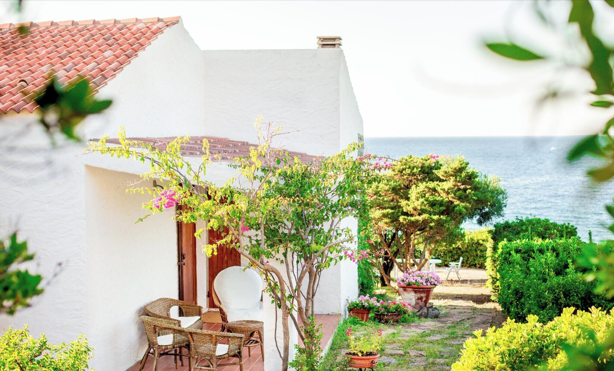 A white building with a tiled roof, a patio with wicker furniture, and potted plants.