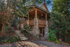 Une cabane avec des fondations en pierre, un revêtement extérieur en bois et une véranda dotée d’une balustrade en pierre.