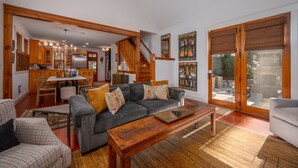 A spacious living area with a grey sofa, wooden coffee table, and a dining table with chairs. A staircase leads to an upper level, and large windows provide natural light. - Mountain Gem I Pet Friendly Luxury Cottage in Cheshire Village (Black Mountain)
