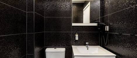 Un baño moderno con pared de azulejos negros, inodoro y lavabo blancos, y un espejo sobre el lavabo.
