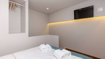 A hotel room with a bed, a flat-screen TV mounted on the wall, and a built-in shelf with towels.