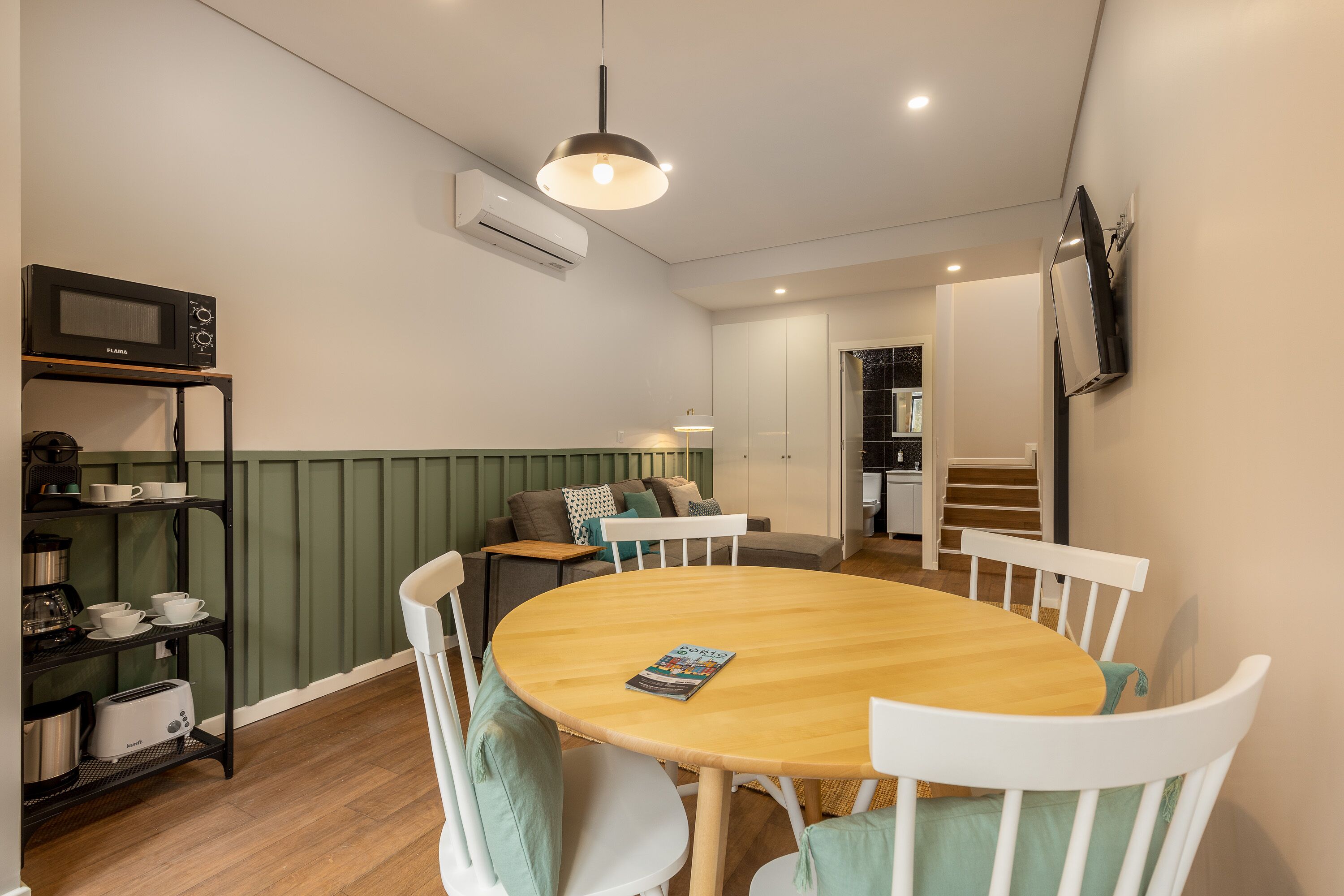 A dining area with a round wooden table, white chairs, and a black shelf with kitchen items.