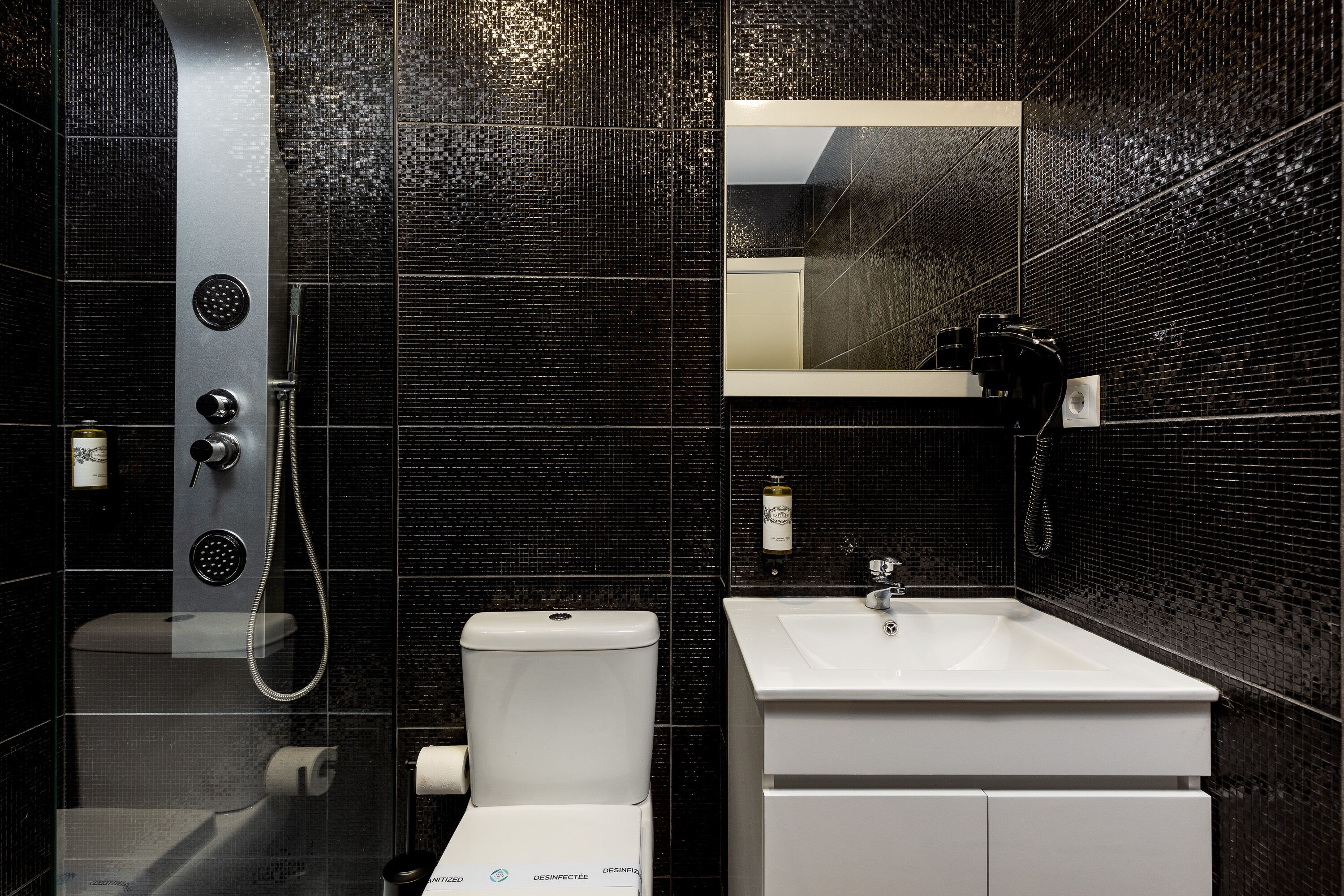 A modern bathroom with a black tiled wall, a white sink, a toilet, and a shower with a handheld showerhead.