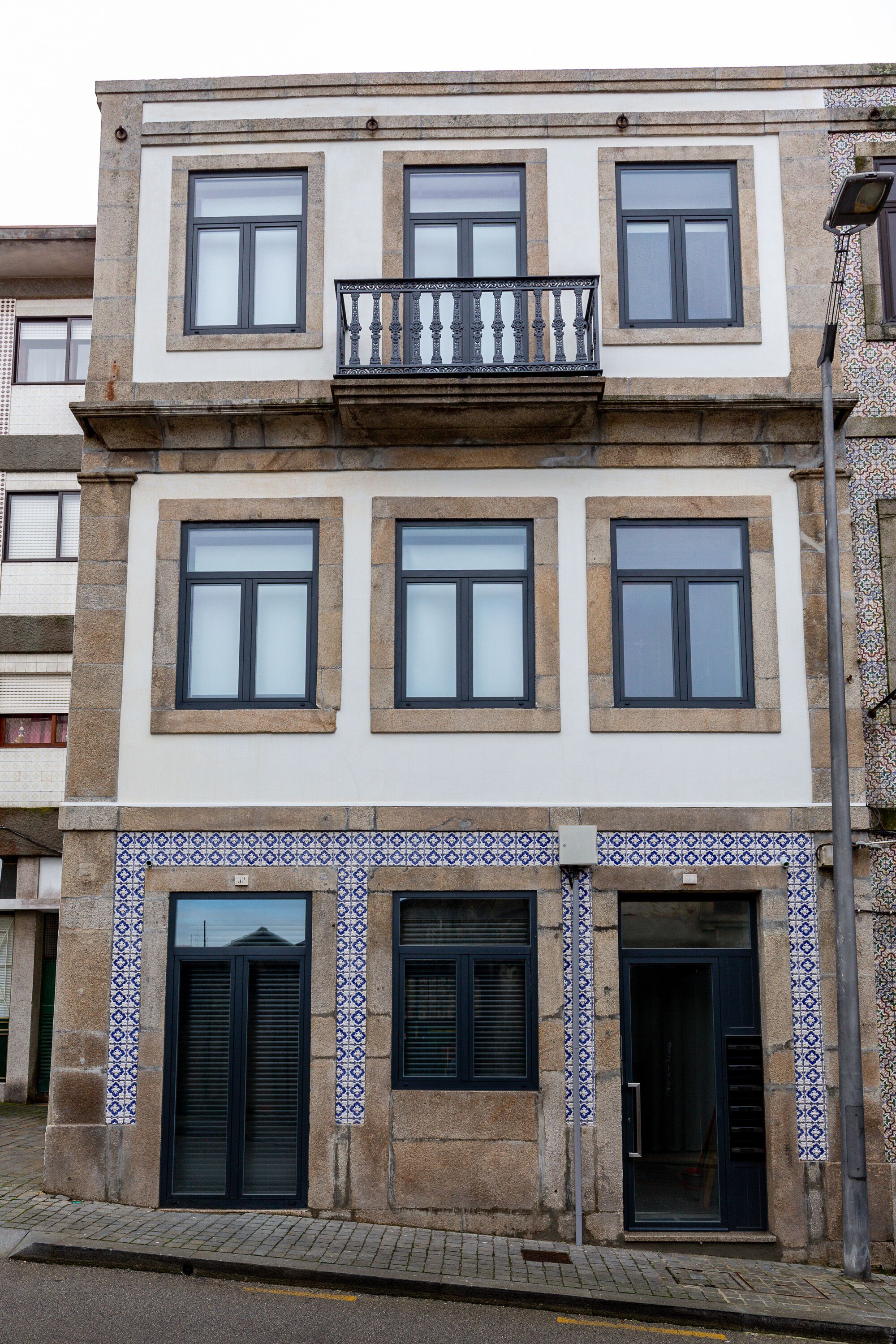 A multi-story building with a balcony on the second floor, a tiled entrance, and a door with a handle.