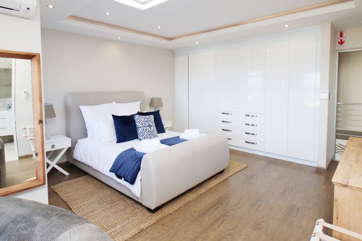 A modern bedroom with a large bed, white wardrobe, and a wooden nightstand.