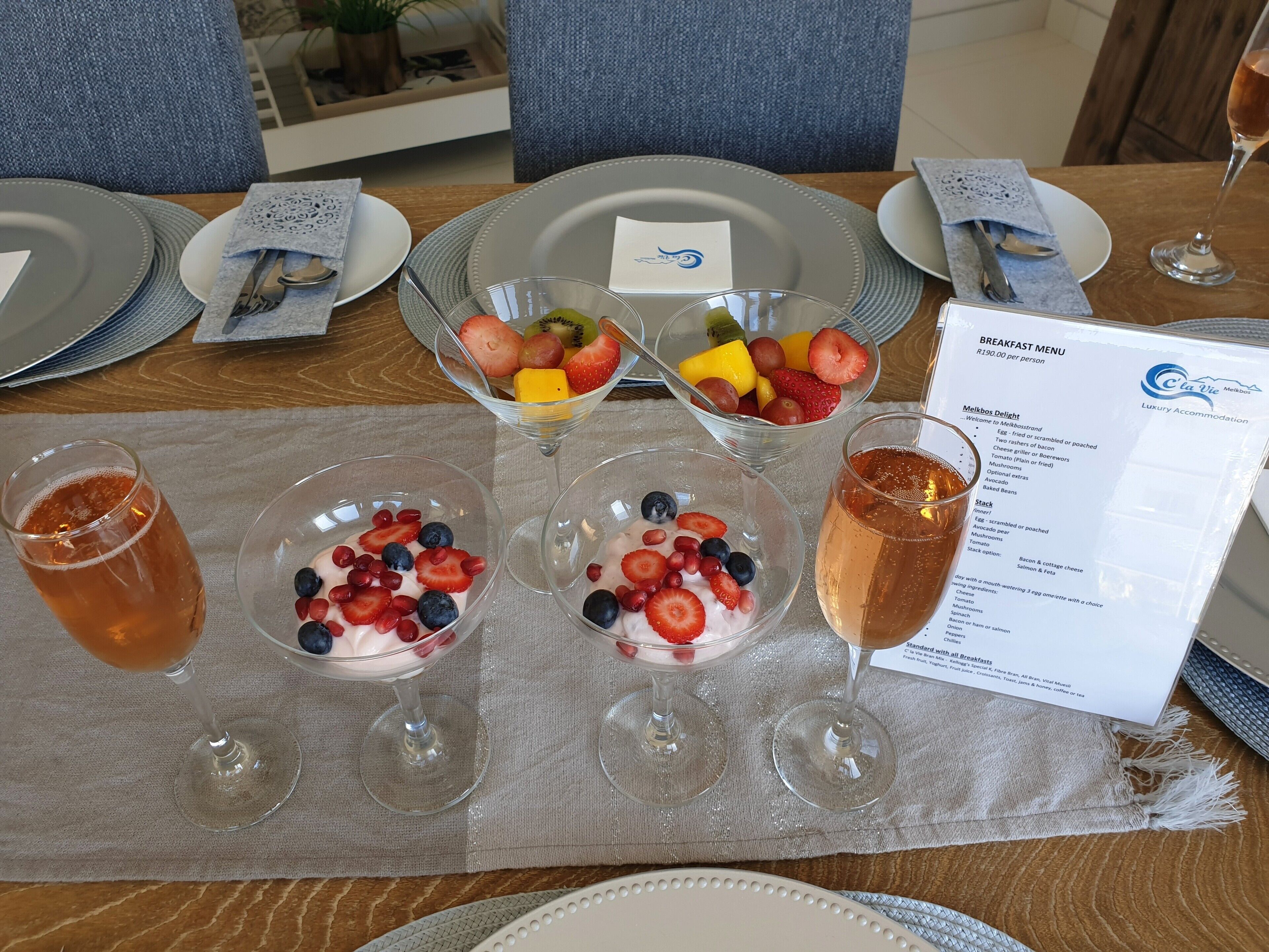Una mesa de desayuno con un menú, cuencos de fruta y vasos de bebidas.
