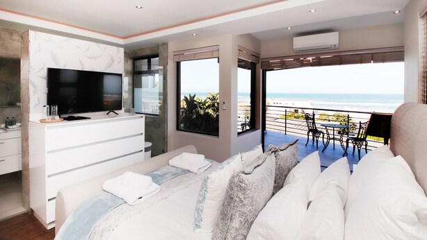 A modern bedroom with a large bed, a TV, and a balcony with a view of the beach. - C' la Vie Melkbos (Cape Town)