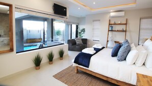 A modern bedroom with a large bed, a TV mounted on the wall, a window with a view of a pool, and a small shelf with decorative items. - C' la Vie Melkbos (Cape Town)
